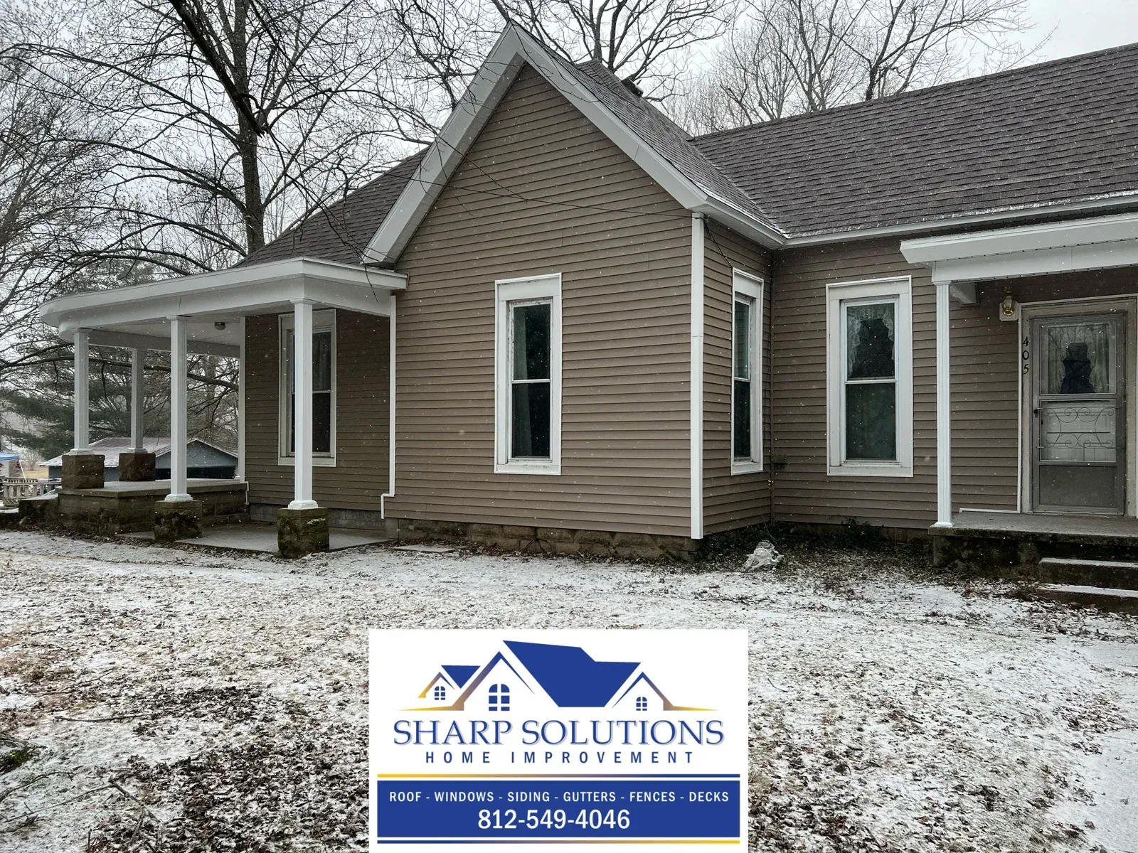 Brown house with white trim and a porch in a snowy yard, with a Sharp Solutions roofing logo overlay.