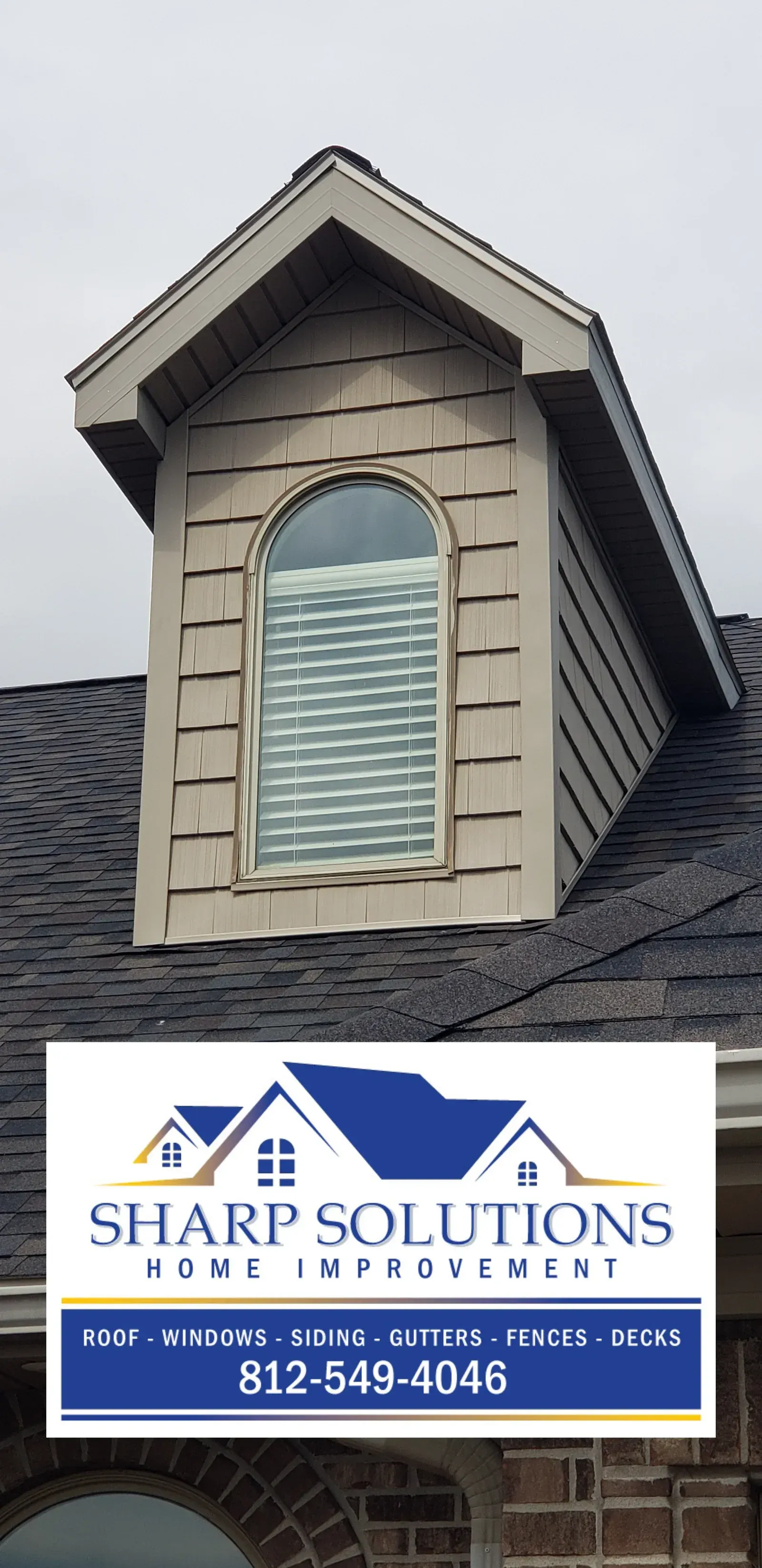 Dormer roof with tan siding and arched window above Sharp Solutions roofing company logo and phone number