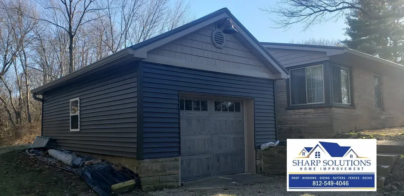 Gray house exterior with garage and front porch, surrounded by bare trees under a clear sky