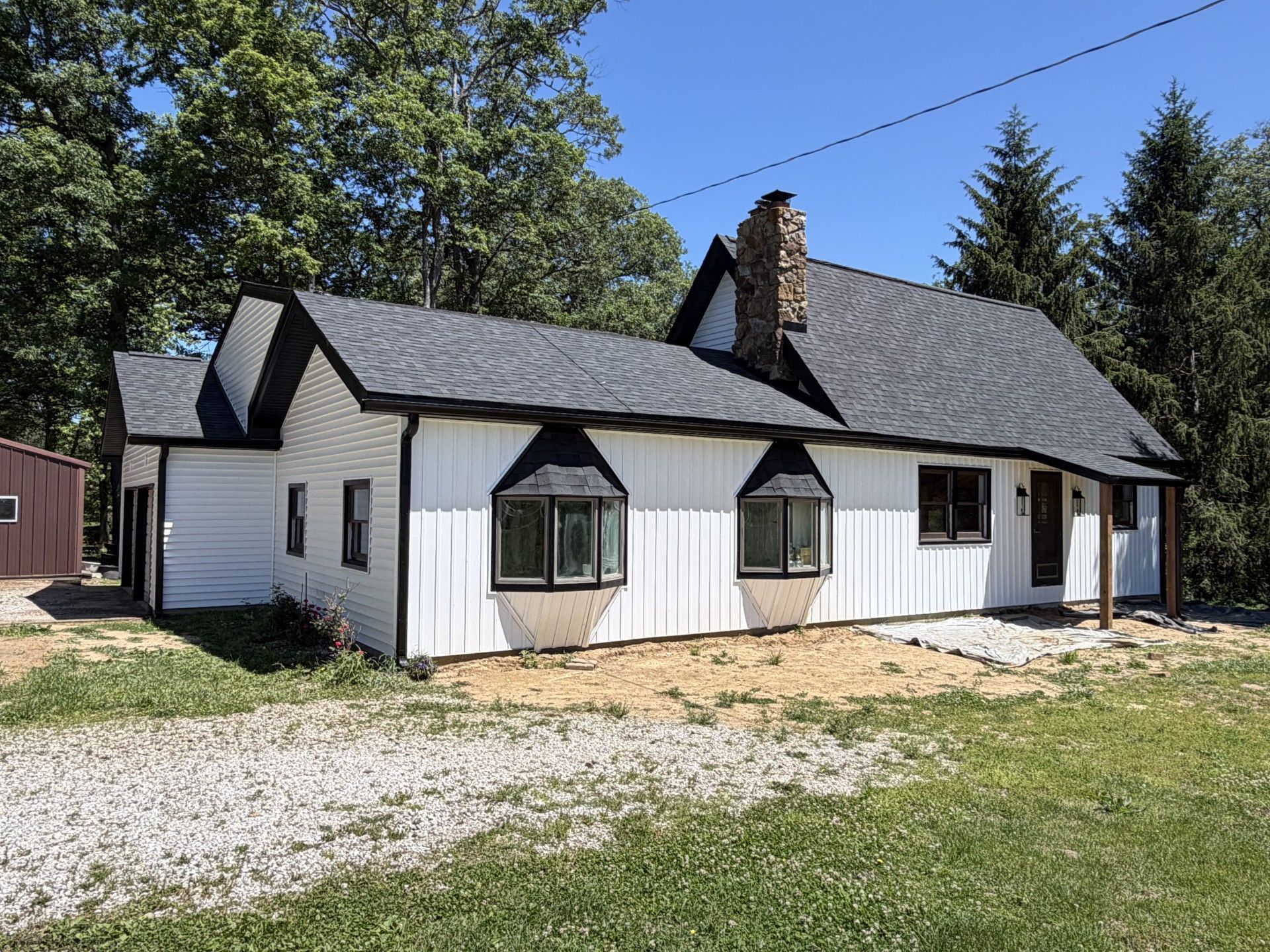 White cottage with gray roof and bay windows on a grassy lot under a clear blue sky