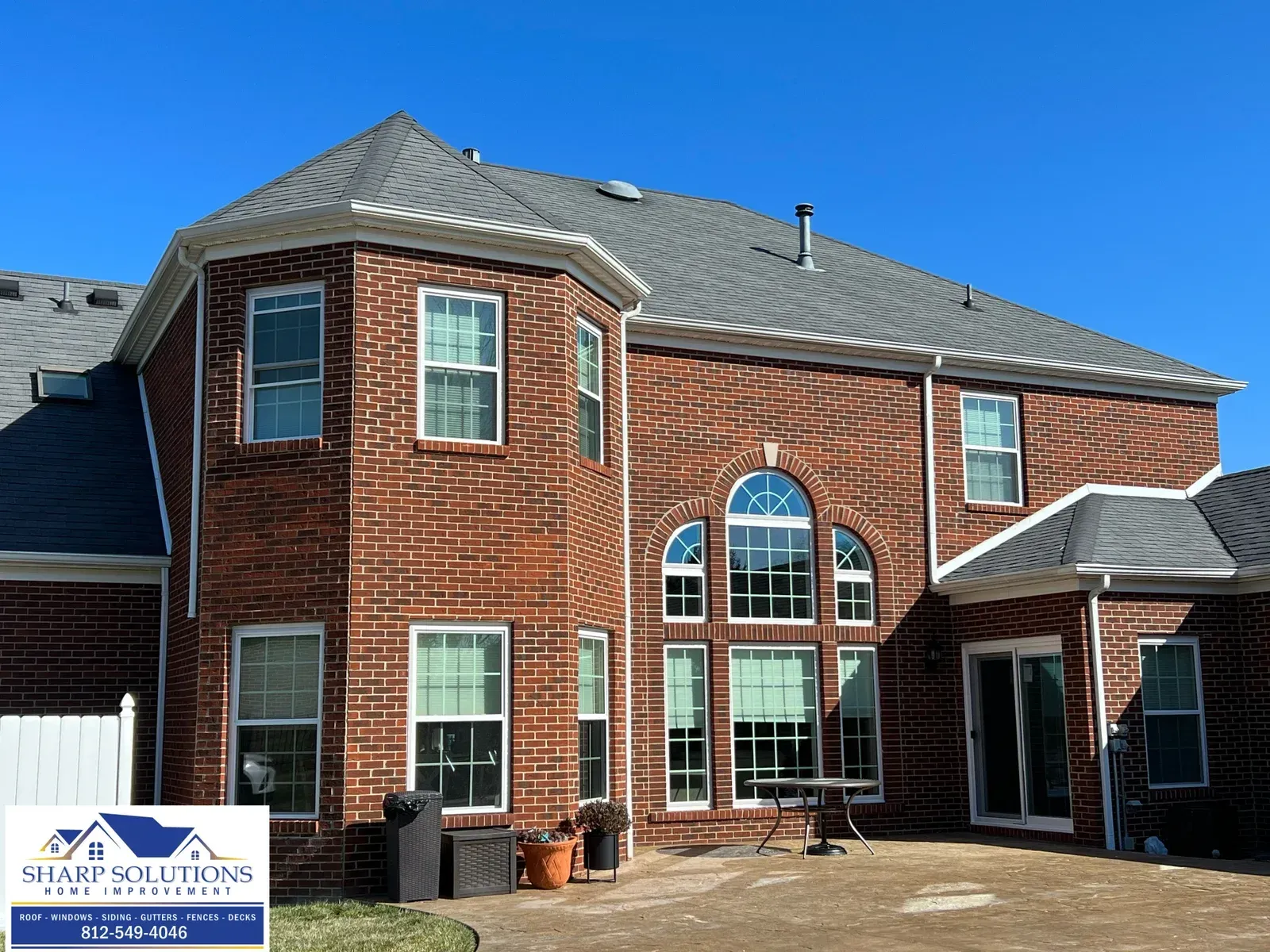 Brick two-story house with white-trim windows, gray roof, and a front porch under a clear blue sky
