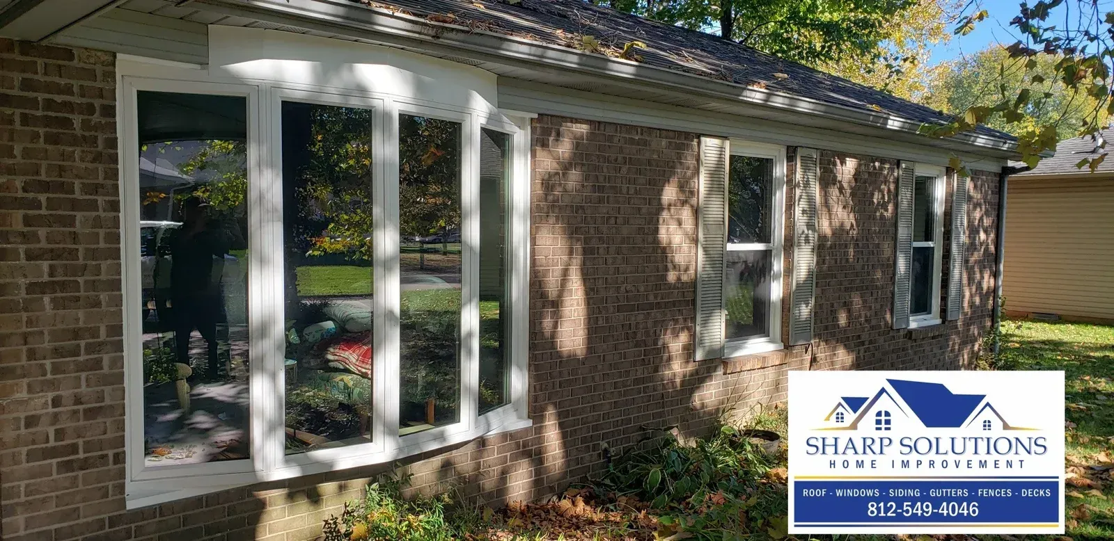 Brick house exterior with white sunroom windows and a Sharp Siding logo in the lower right.