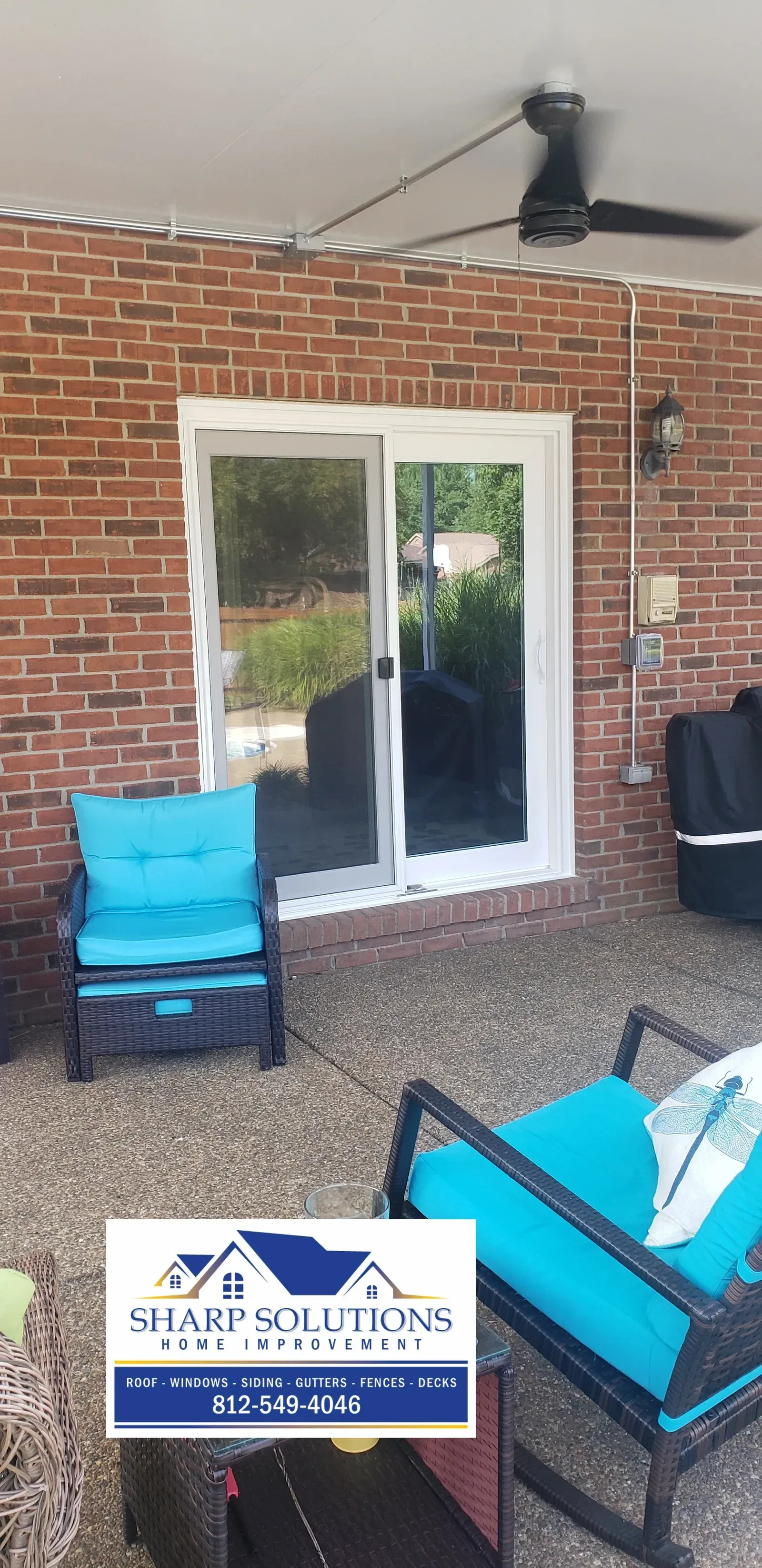 Brick patio with white French doors, ceiling fan, blue chairs, and a patio sign