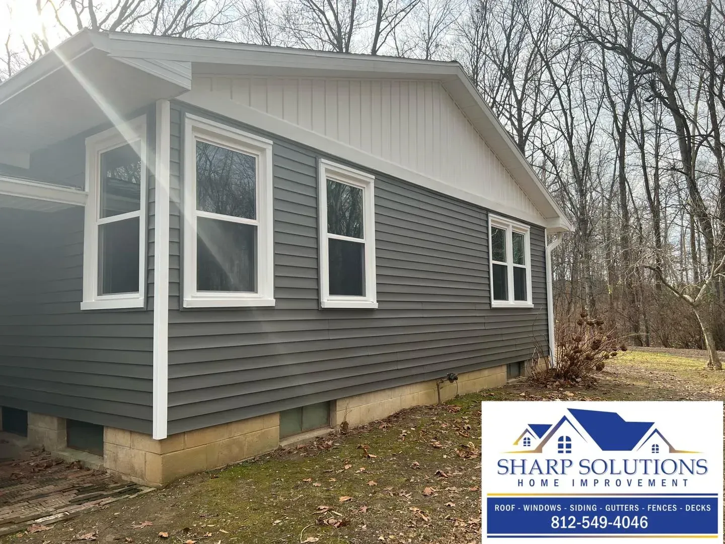 Gray house with white trim and bay windows in a wooded yard, with Sharp Solutions logo at bottom right