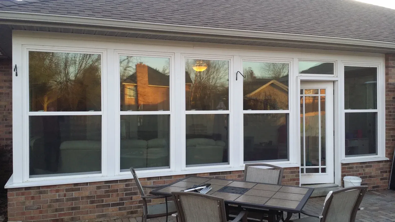 Outdoor patio with white-framed windows and glass door on a brick house, with a table and chairs in front.