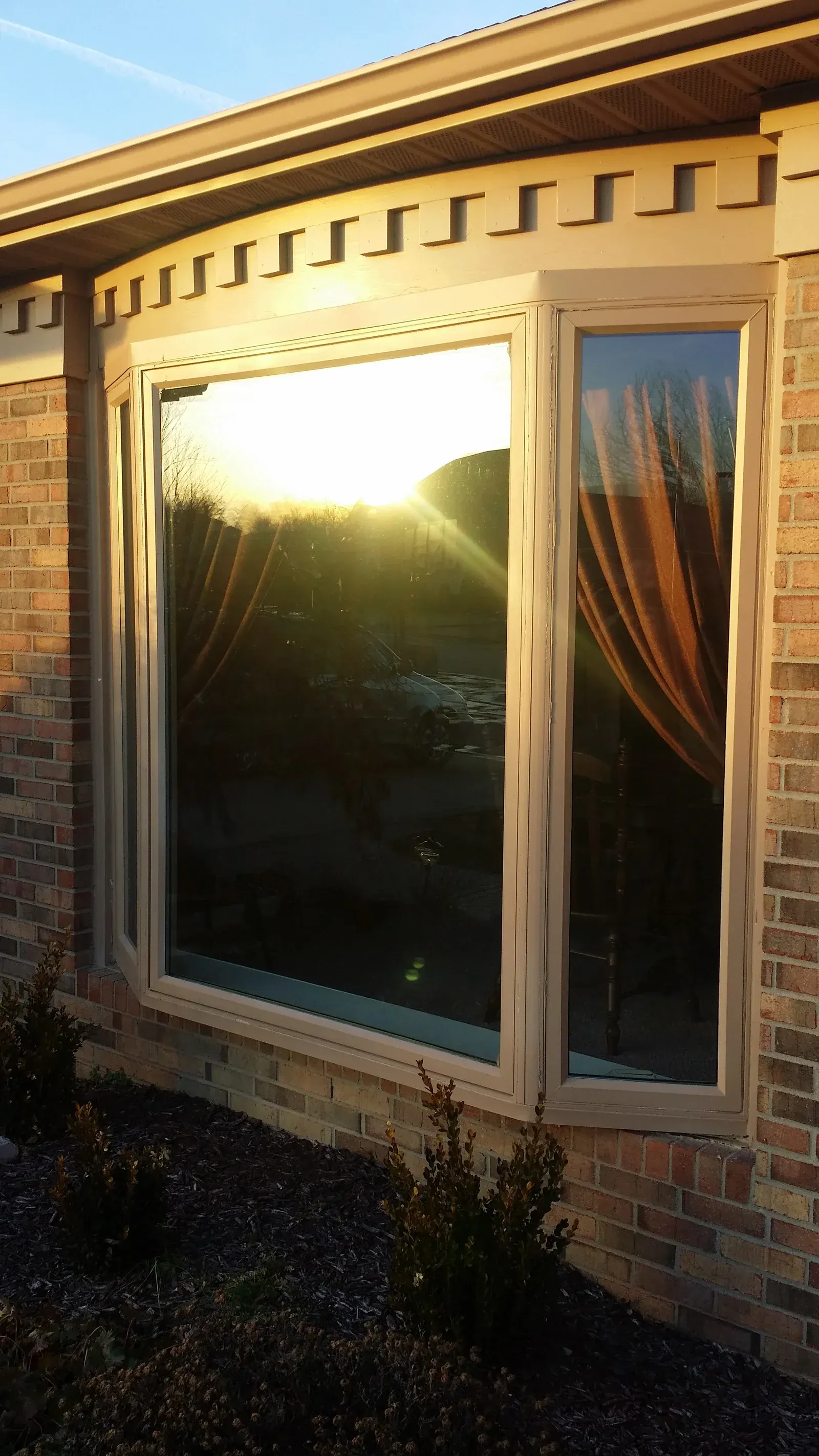 Sunlit brick house window with beige trim and curtains inside