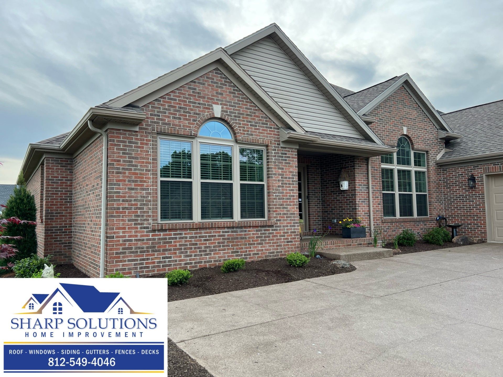 Brick suburban house with arched windows, front porch, and driveway under cloudy sky