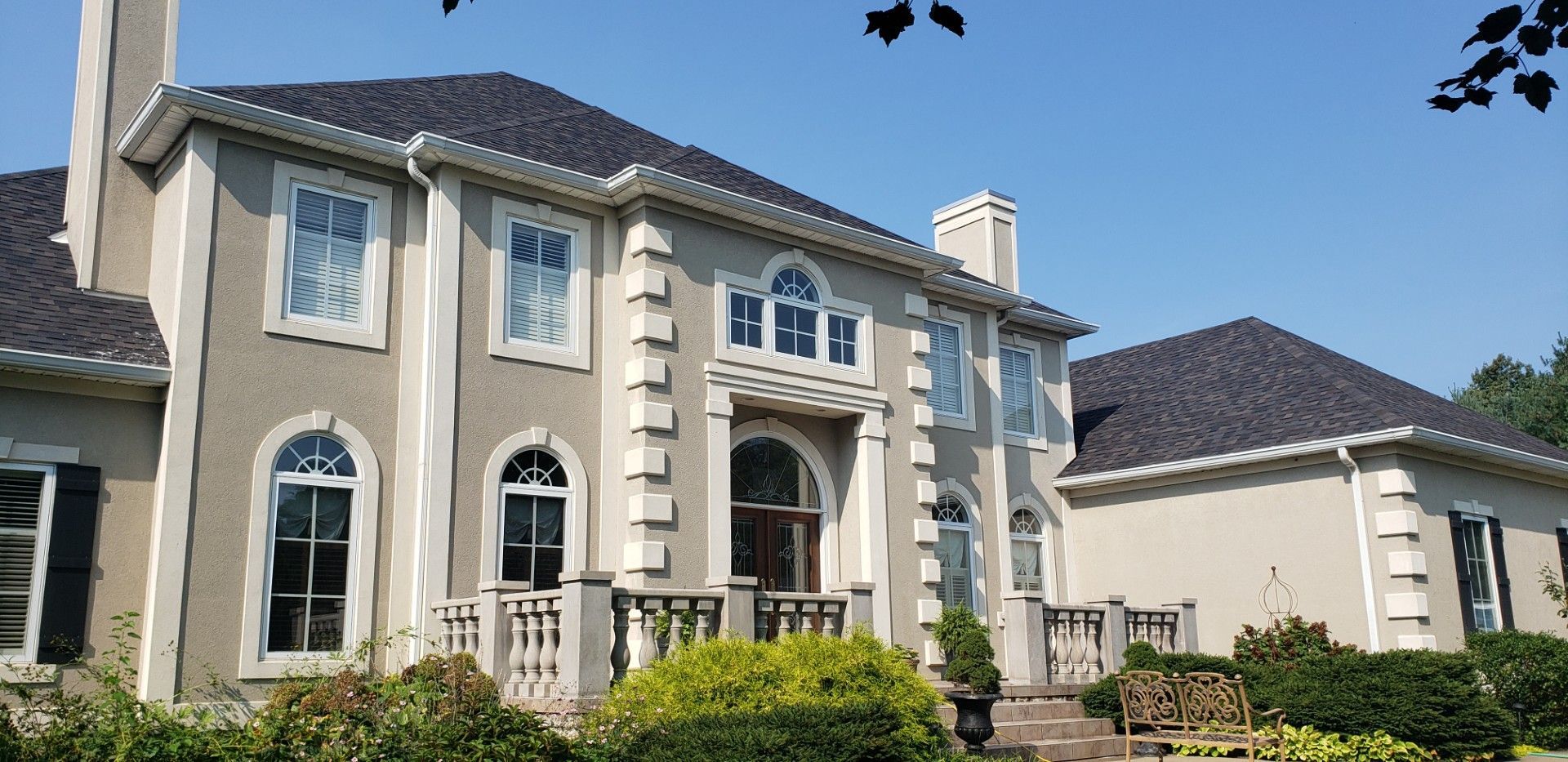 Large beige two-story Mediterranean-style house with arched windows and a tiled roof under a clear blue sky
