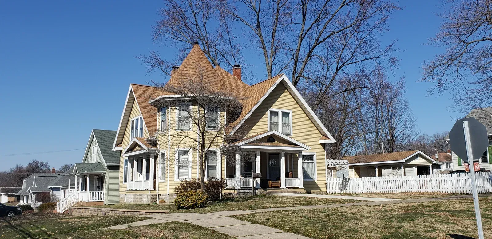 Victorian-style yellow house with white trim and a front porch in a sunny neighborhood yard