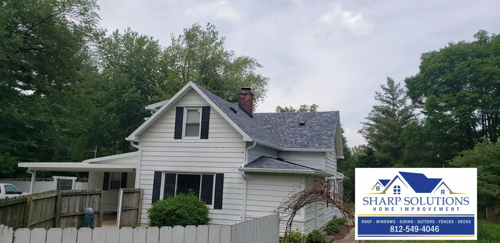 White two-story house with damaged siding and roof, beside a fenced yard and trees; Sharp Solutions logo overlay