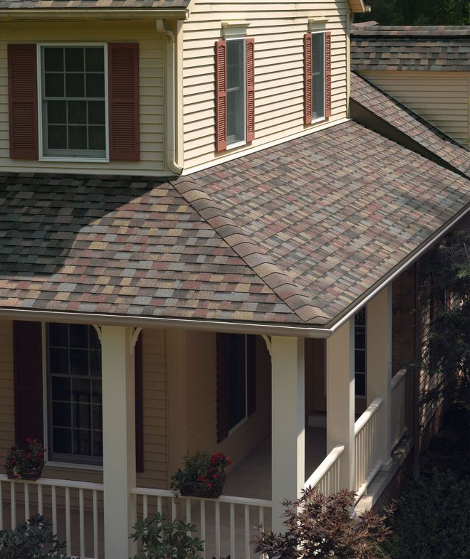 Two-story house with gray shingle roof, tan siding, red shutters, and a covered porch.