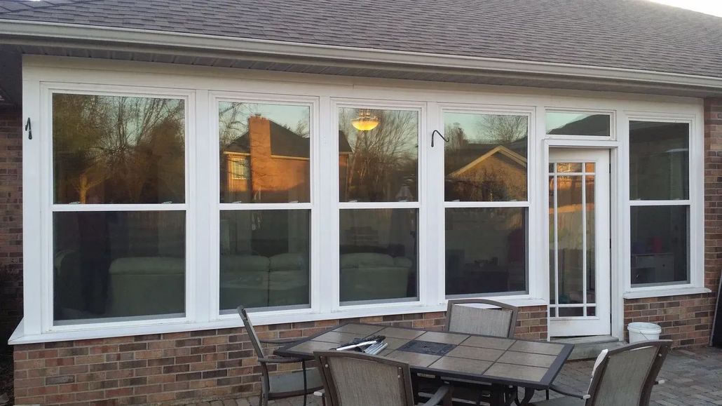 Patio with outdoor table and chairs in front of a white house wall with large windows and a glass door.