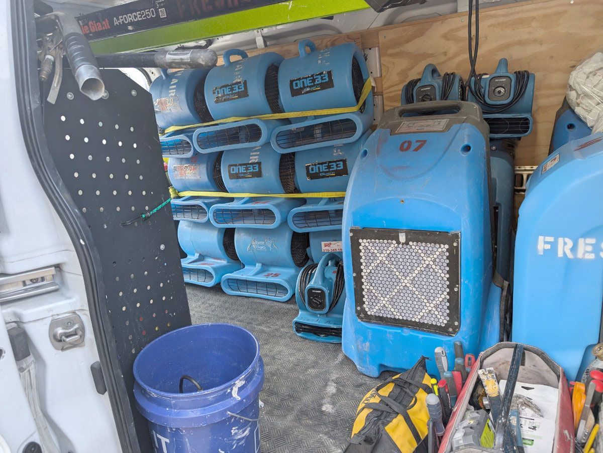 Inside of a work van packed with blue industrial dehumidifiers, air movers, a blue bucket, and equipment bags.