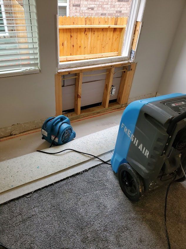 A room undergoing water damage restoration with industrial drying fans placed near an exposed, open wall section.