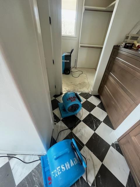 Two blue industrial air movers and a dehumidifier drying a room with a black-and-white checkered floor.
