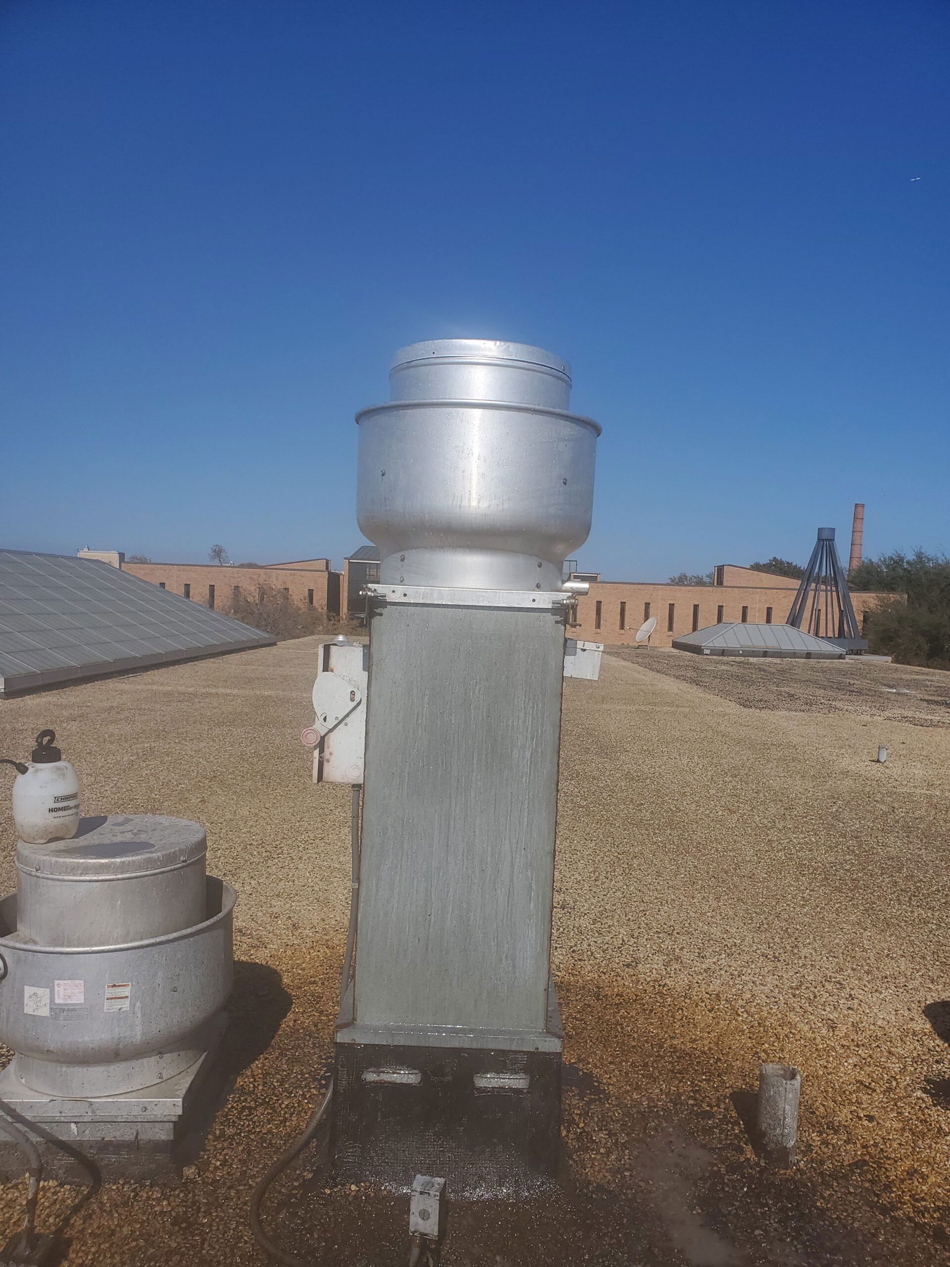 Two metal exhaust vents on a gravel rooftop under a clear blue sky.