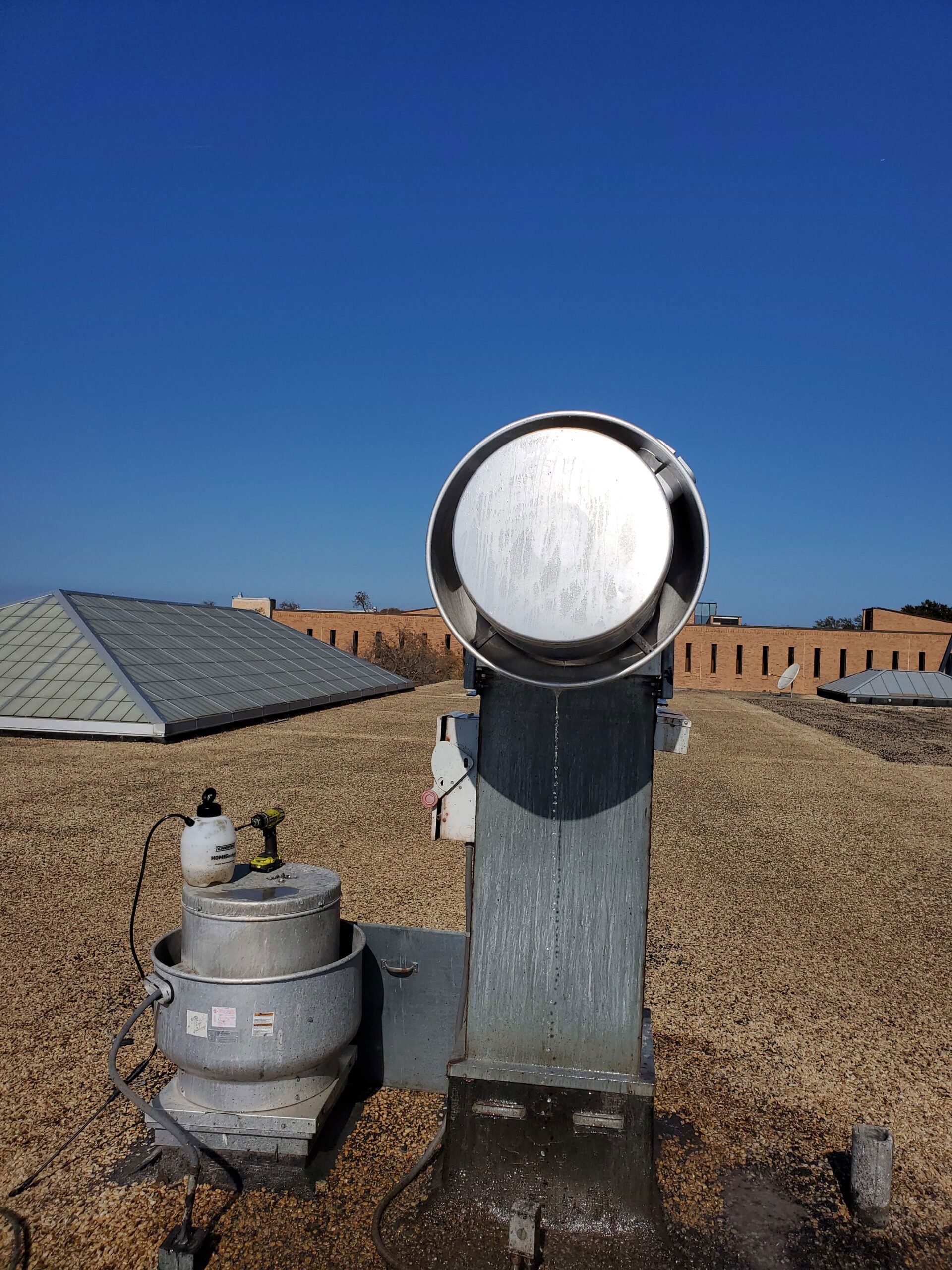 Two HVAC exhaust fans on a gravel-covered rooftop against a bright blue sky.