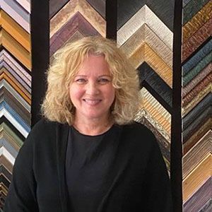 A woman is standing in front of a wall of picture frames.