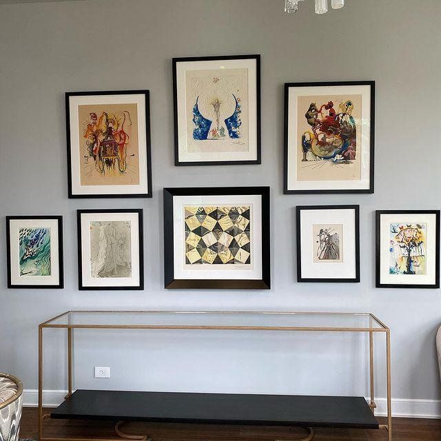 A collection of framed pictures hangs on a wall above a glass table