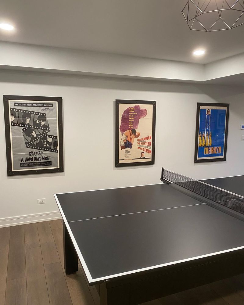 A ping pong table in a room with three posters on the wall.