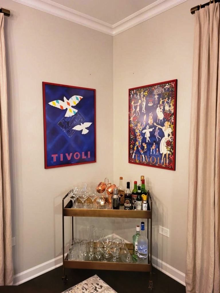 A room with a bar cart and two paintings on the wall.