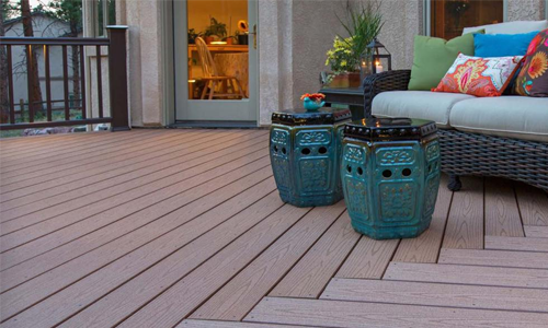 A wooden deck with a couch and two blue stools on it.