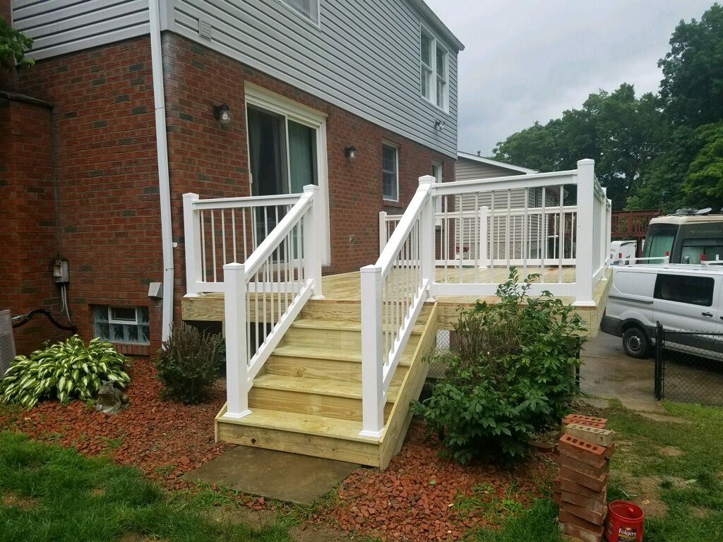 A wooden deck with white railings and stairs is in front of a brick house.