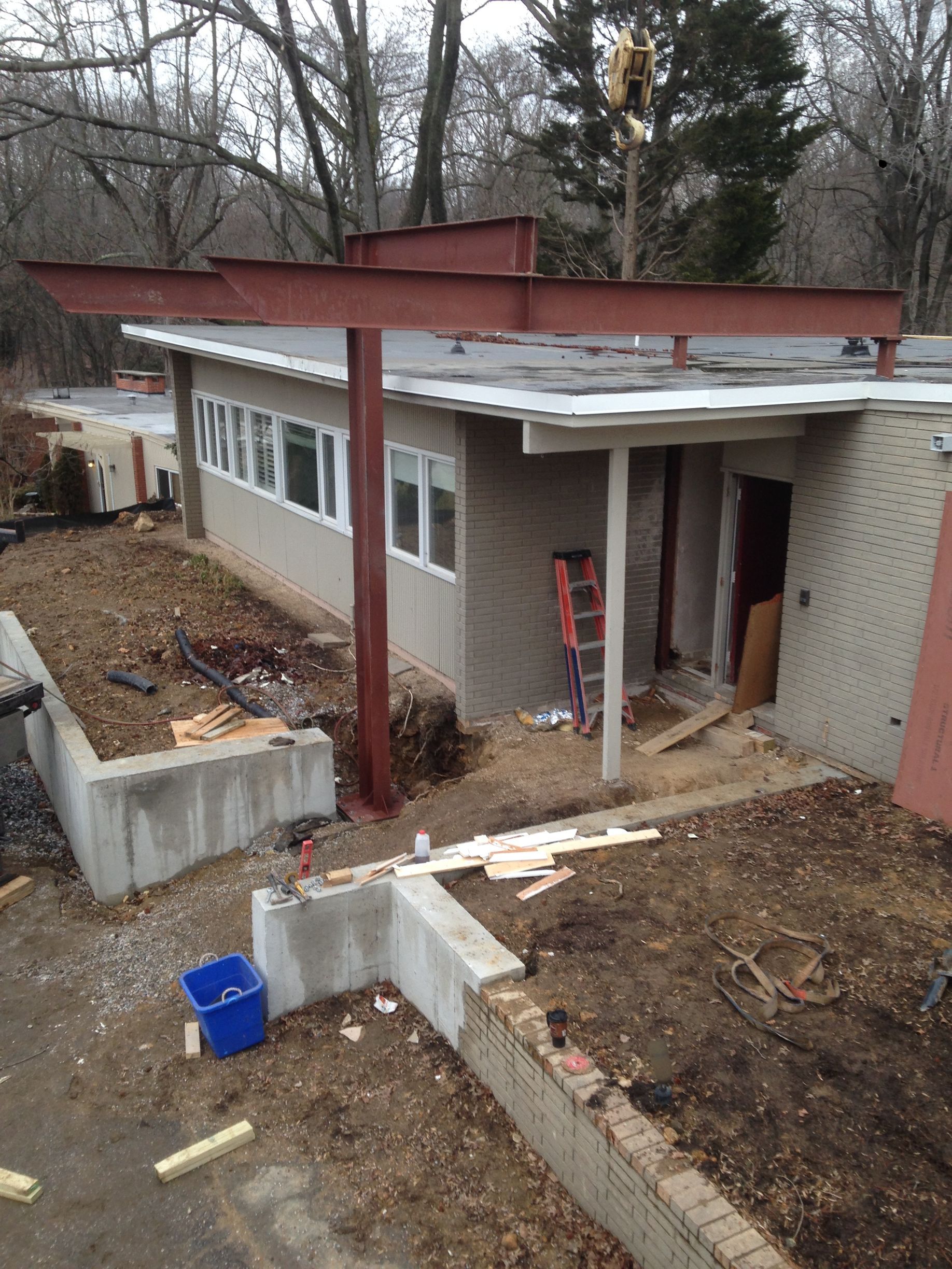 A view of a house undergoing renovations, featuring a newly installed reddish-brown steel support beam on a concrete site.