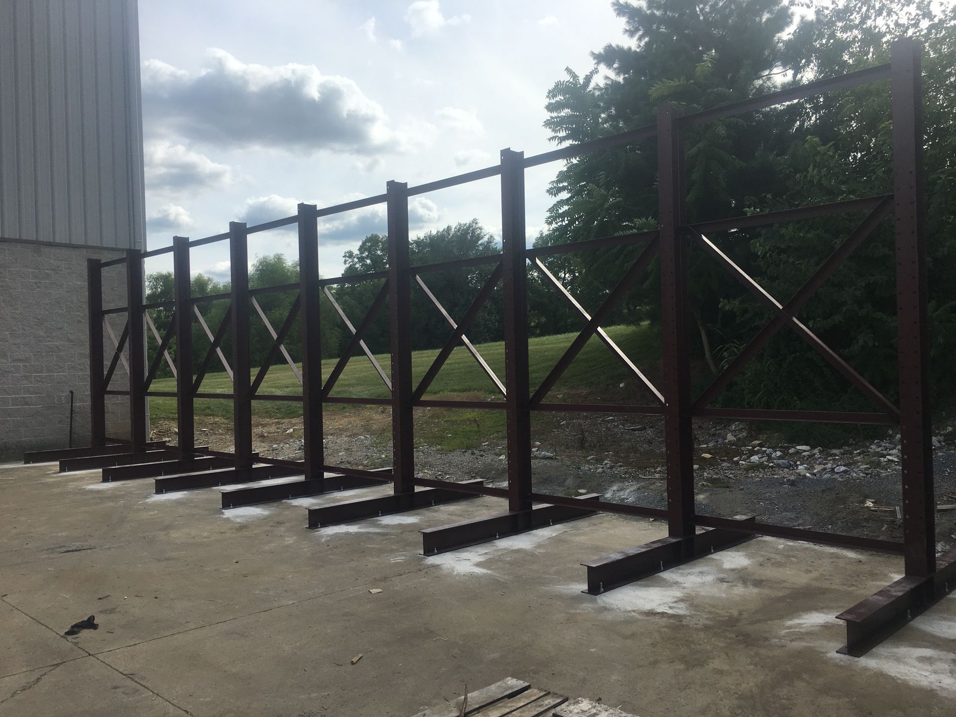 A row of dark metal structural frames with X-bracing, anchored to a concrete slab outdoors.
