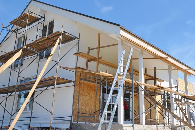 House under construction with scaffolding and ladders against a blue sky