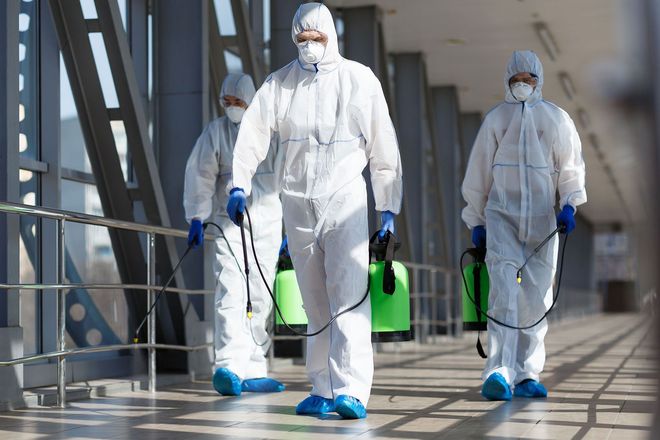 Workers in white hazmat suits disinfecting a floor in a bright industrial corridor