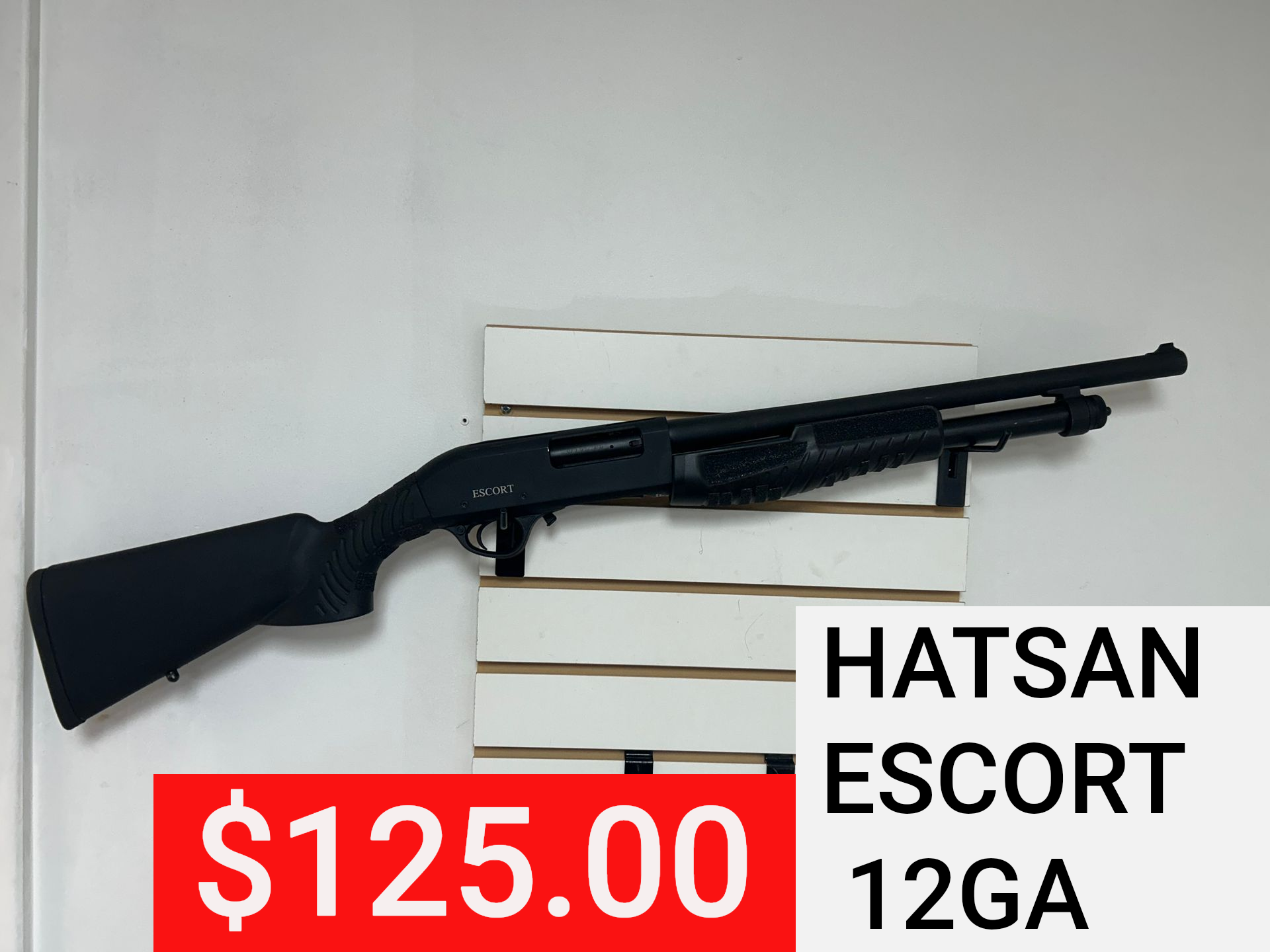 Black Hatsan Escort 12GA shotgun on white wall display, priced at $125.