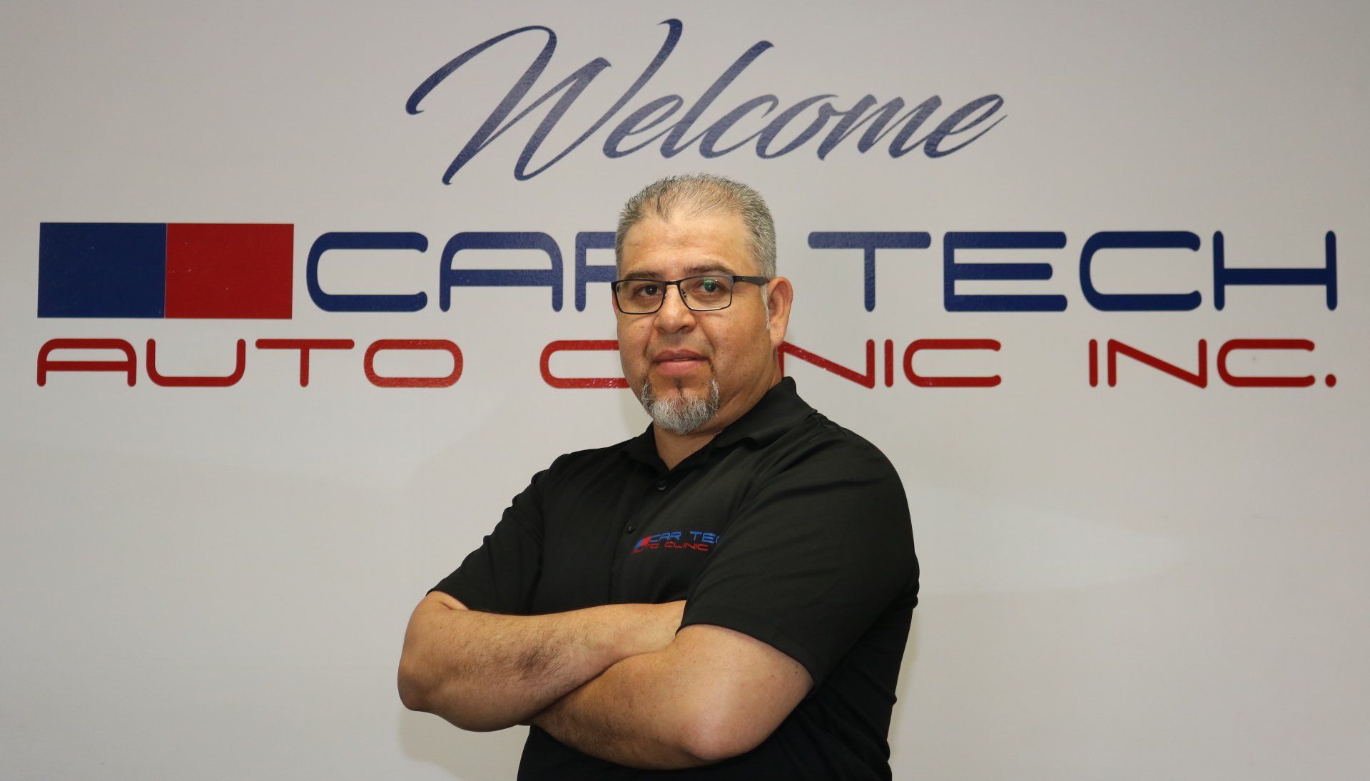 A man is standing in front of a sign that says welcome car tech auto clinic inc.
