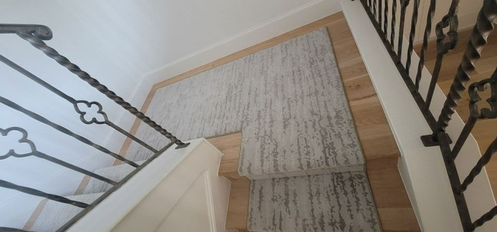 A staircase with a rug on the floor and a wrought iron railing.