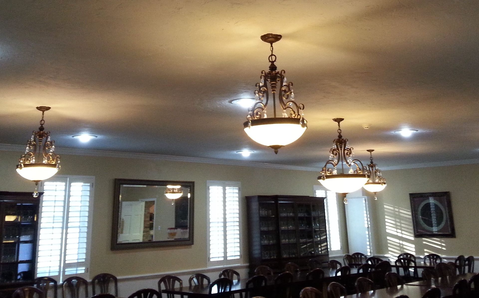 Ornate chandeliers in a dining room, with large table and chairs. Windows and a mirror are visible.