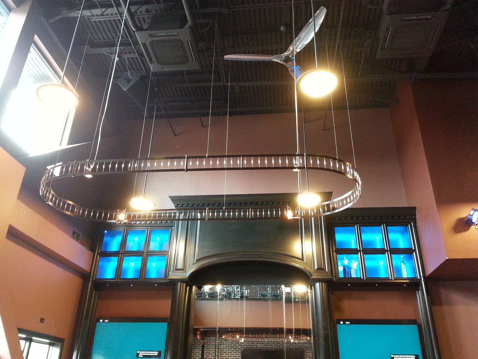 Ceiling fan and oval light fixture above blue-lit architectural details in a commercial space.