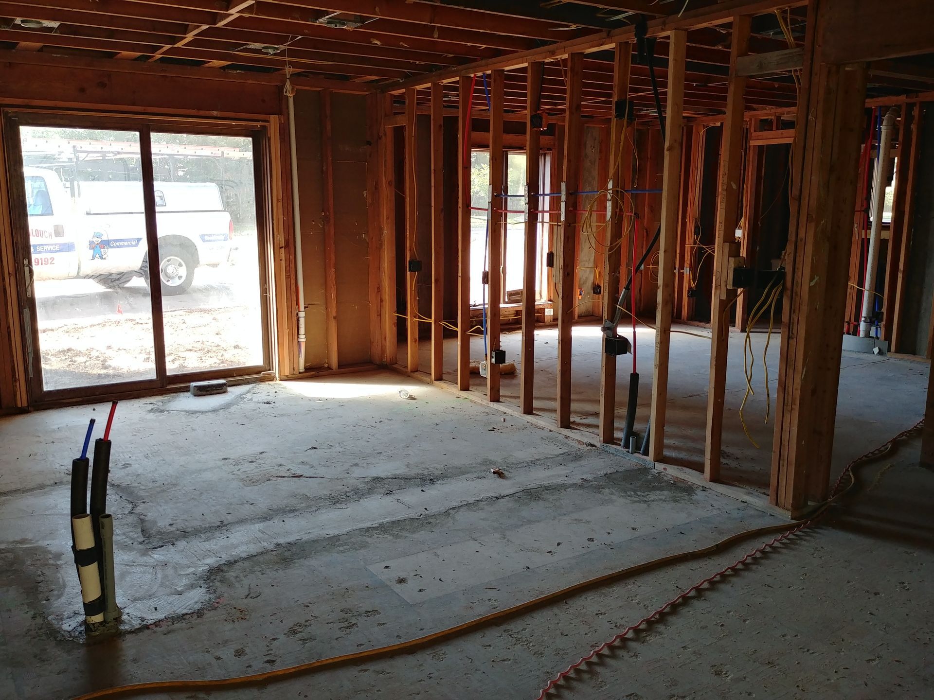 Interior view of a building under construction, showing wooden framing, plumbing, and a concrete floor.