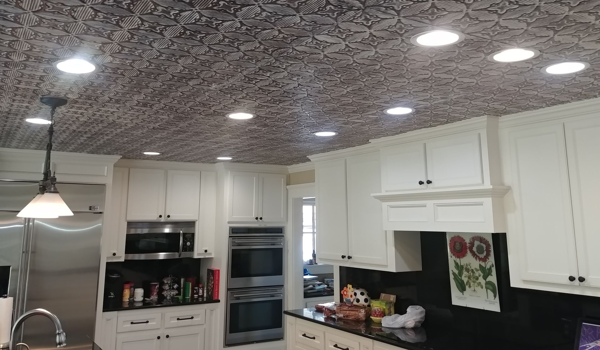 Kitchen with white cabinets, black countertop, patterned ceiling, and recessed lighting.