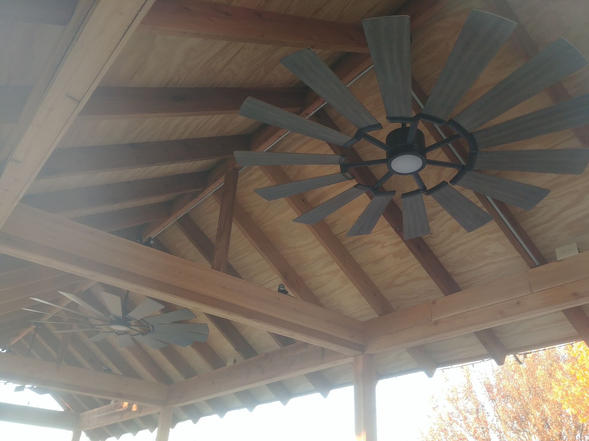 Wooden gazebo ceiling with two large, gray ceiling fans and exposed beams.