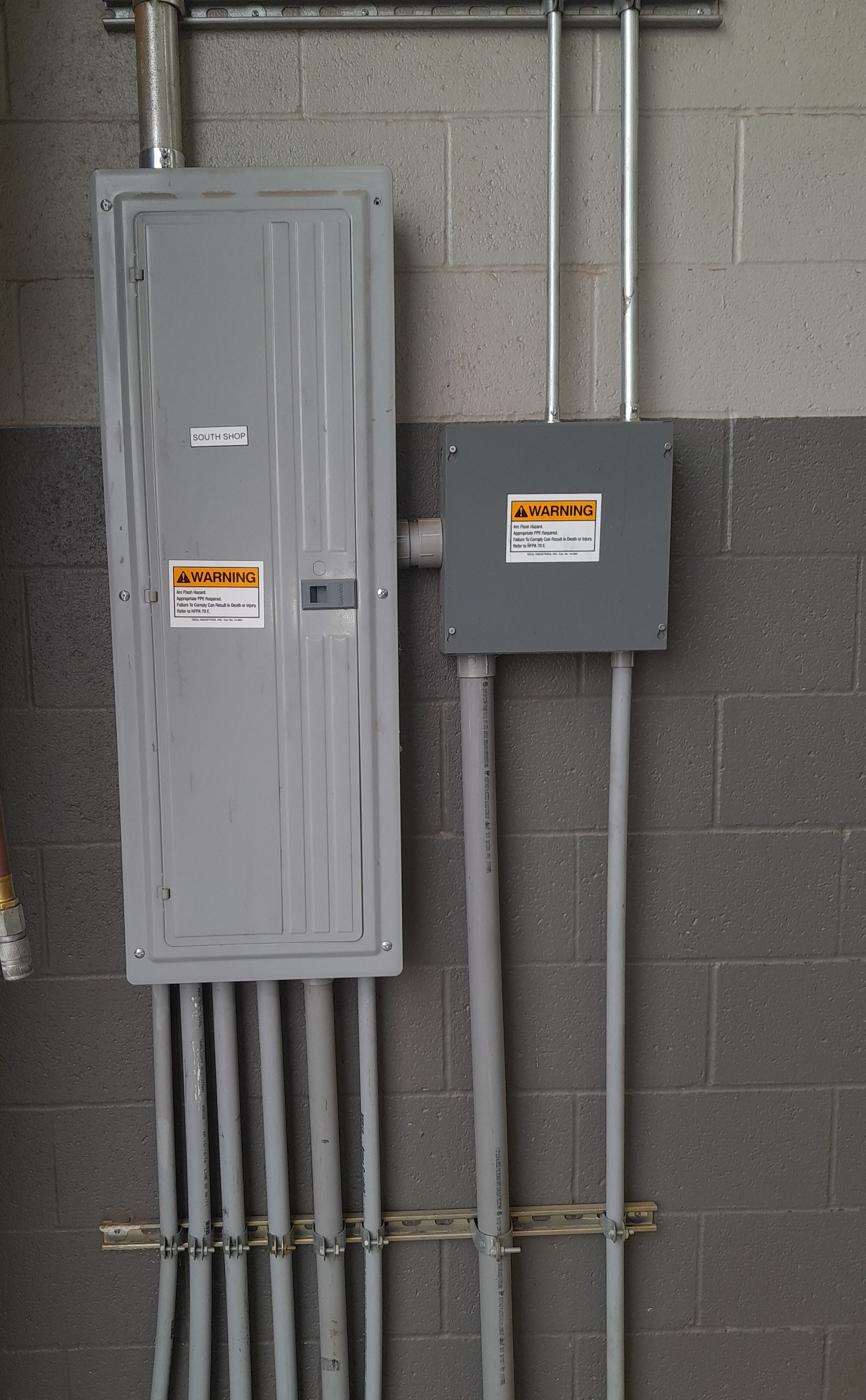 Electrical panel and junction box mounted on a brick wall with conduit running to each.