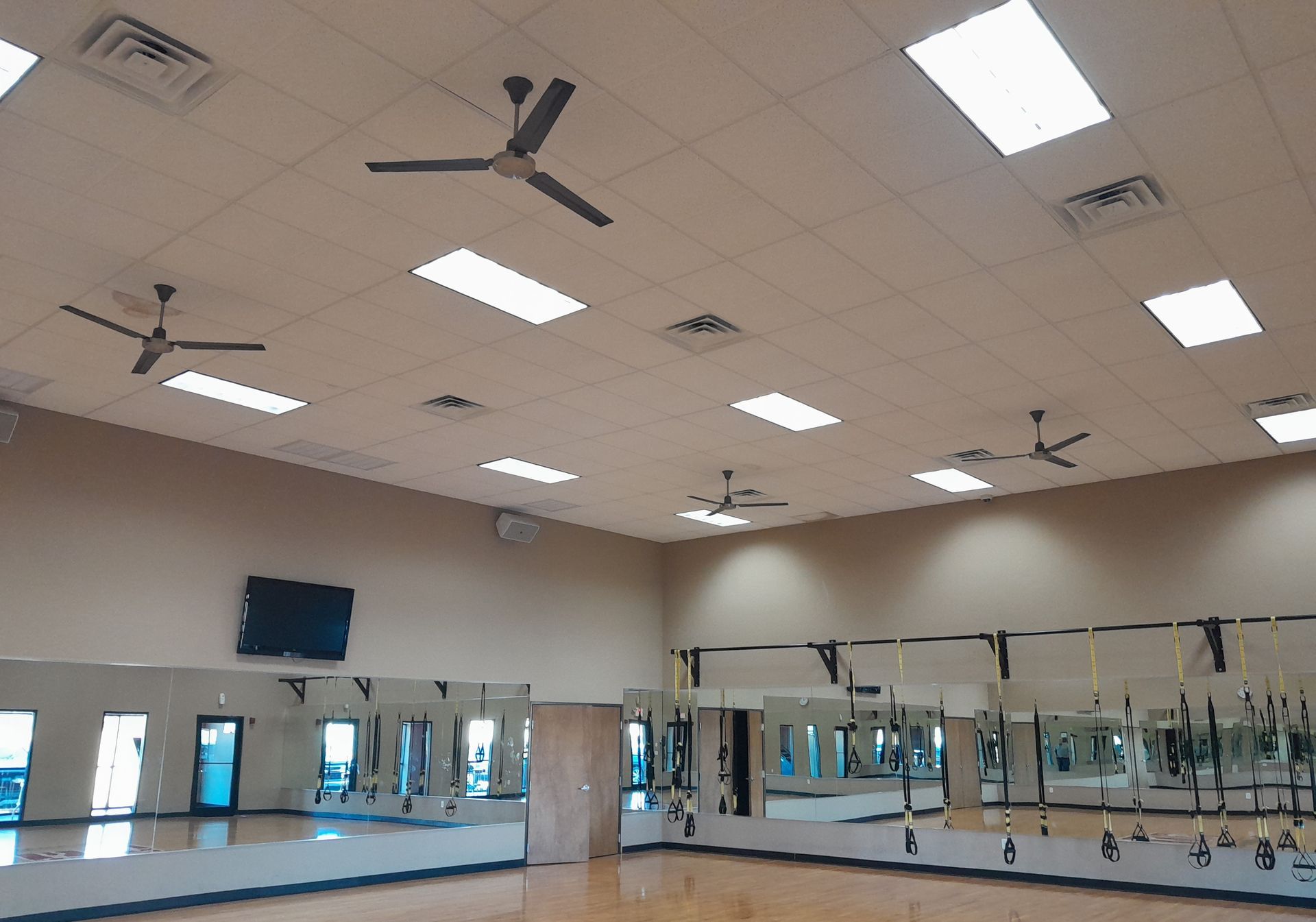 Gym interior with mirrors, ceiling fans, and overhead lights.
