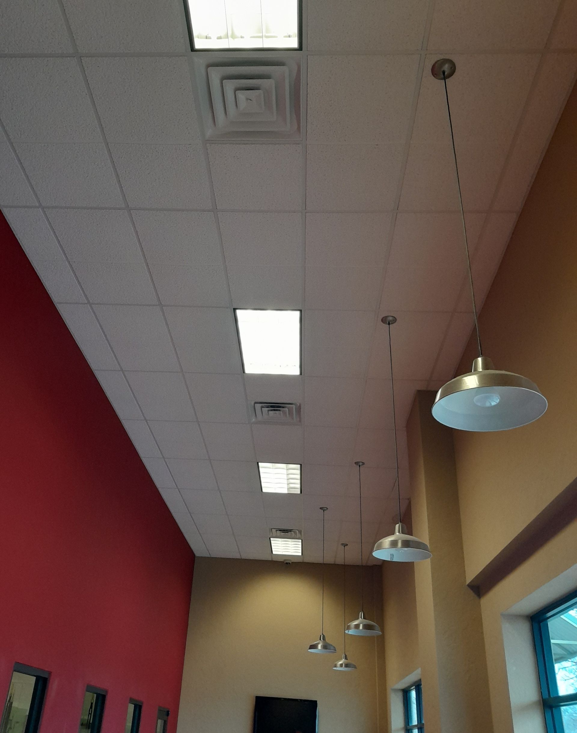 Interior view of a building's ceiling, with recessed lighting and hanging pendant lights over red and tan walls.