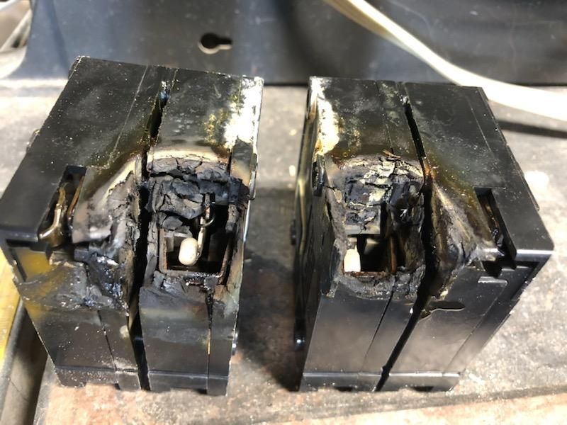Two severely damaged electrical circuit breakers, black with charring and melting.