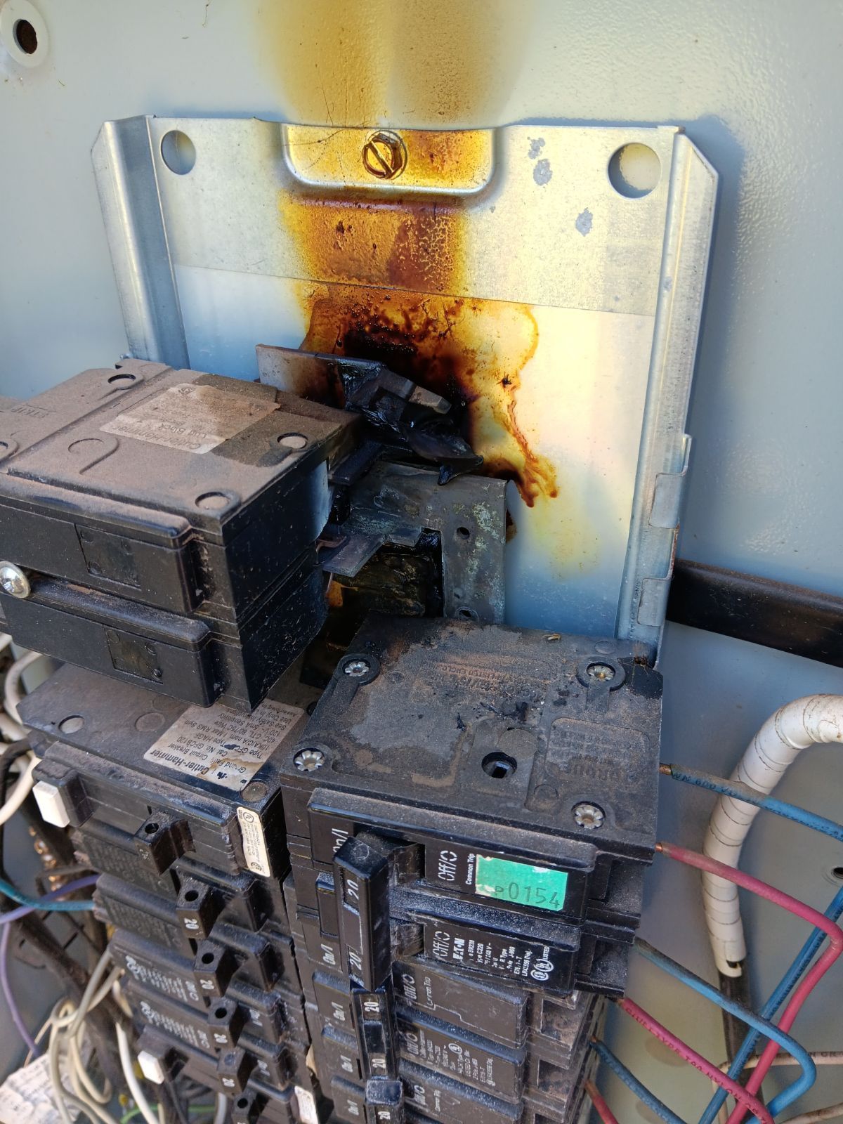 Electrical panel with burnt wiring and components; brown burn marks visible on the metal panel.