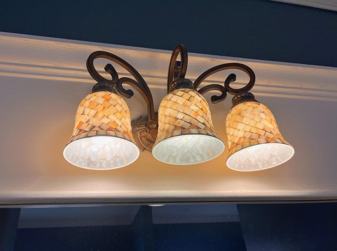 Three-light sconce with amber mosaic glass shades and ornate bronze fixture on a white wall.