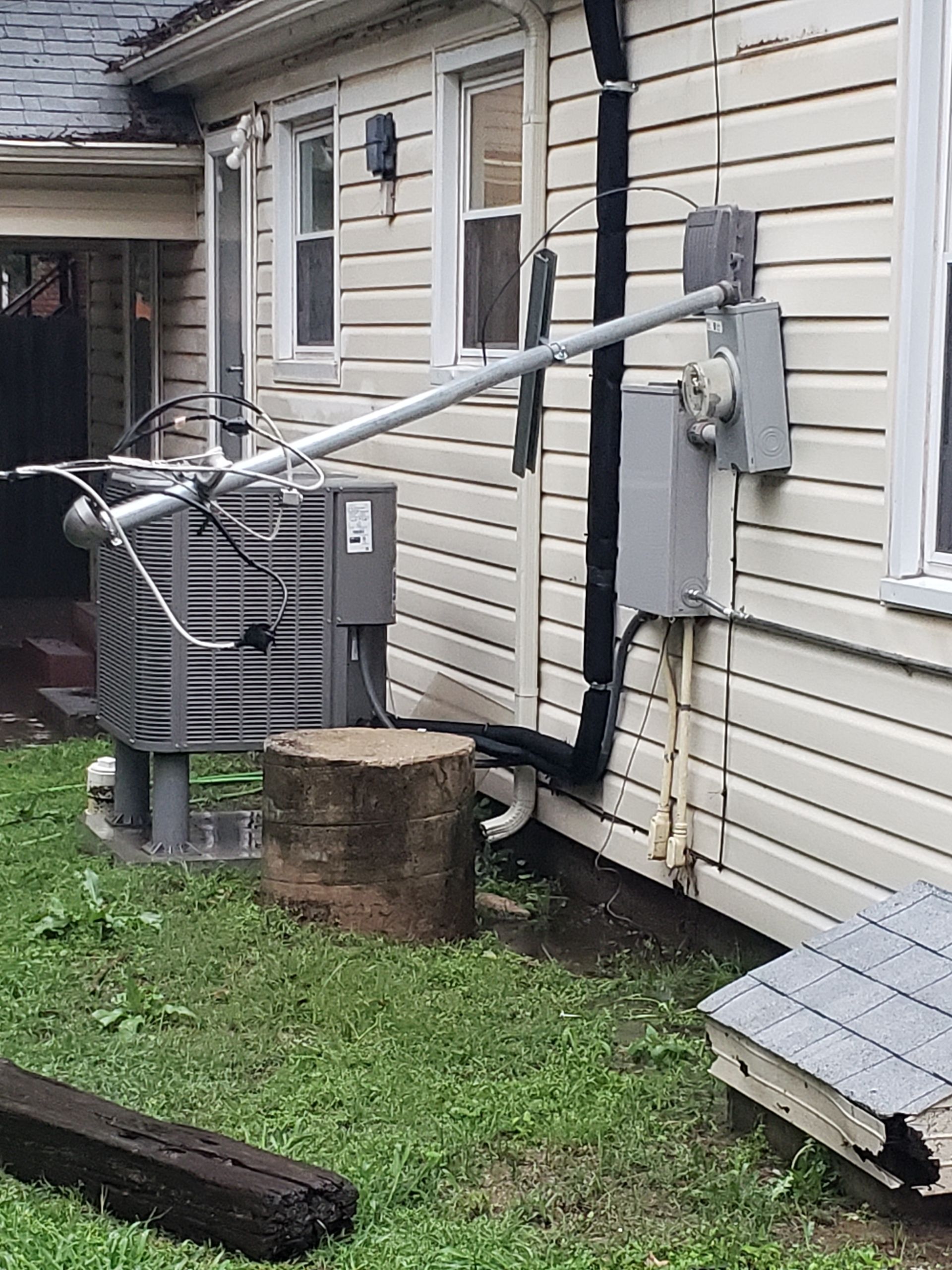 Exterior of a house with an air conditioning unit and electrical components attached to the side. Gray, white, and black.