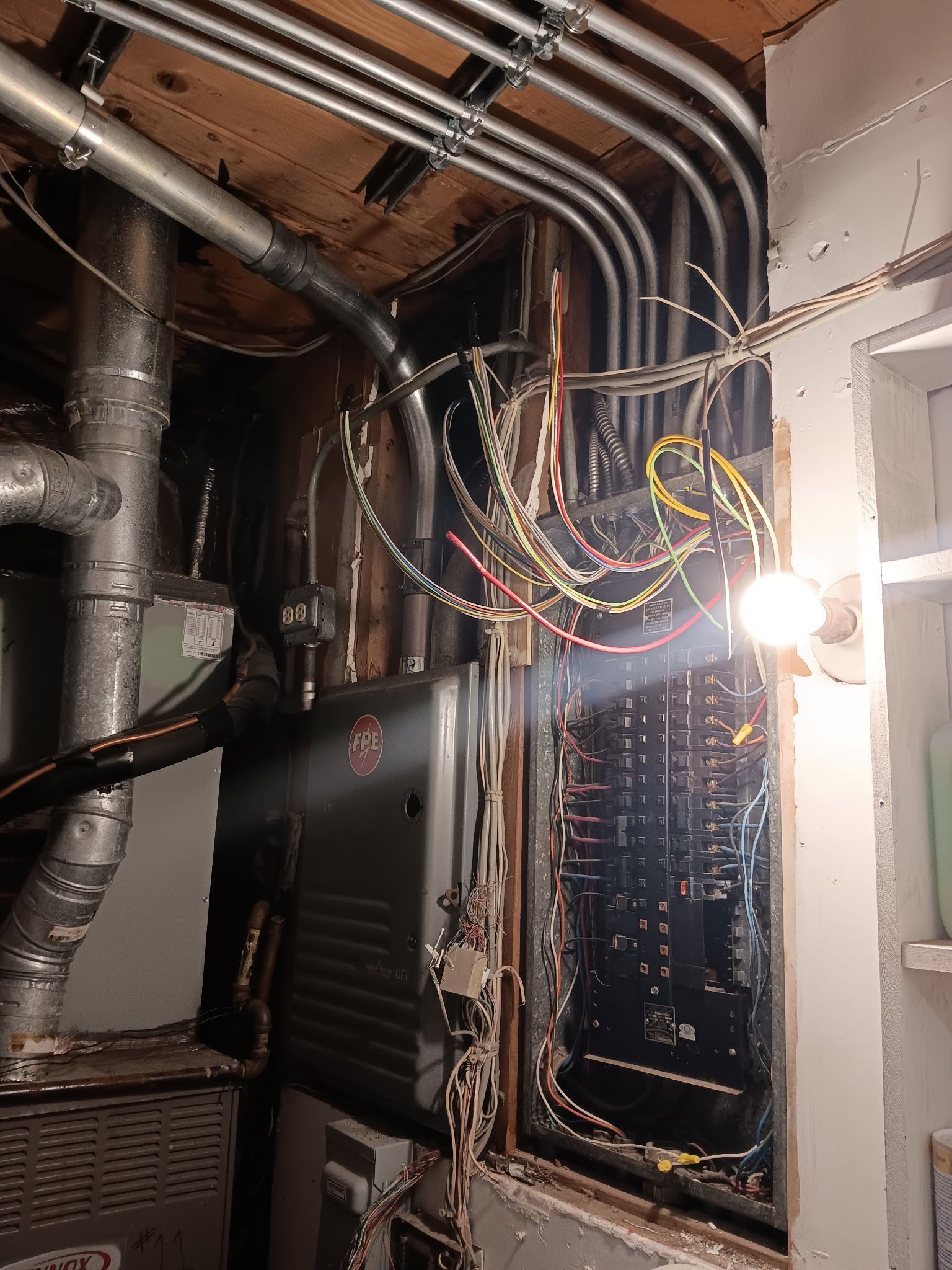 Electrical panel with exposed wiring and conduit in a cluttered space.