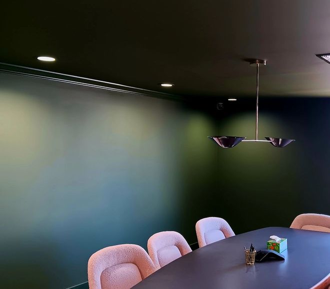 Conference room with dark green walls, pink chairs, and a black table. Modern chandelier and recessed lighting.