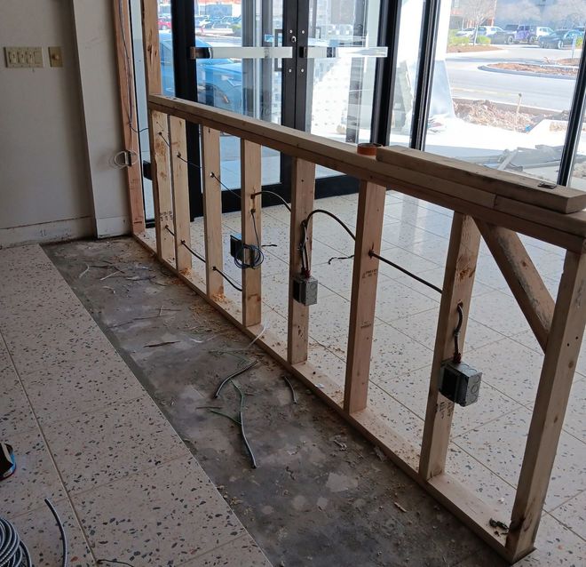 Interior during construction. Wooden frame with electrical boxes and wiring. Flooring is exposed concrete and tile.