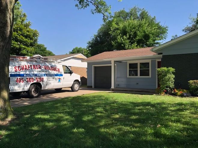 White van parked in front of a blue house with a garage. Lush green lawn with trees.
